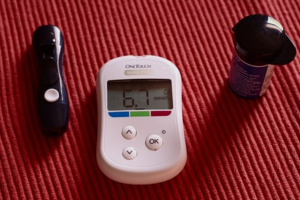 A blood glucose meter sitting on top of a red surface.