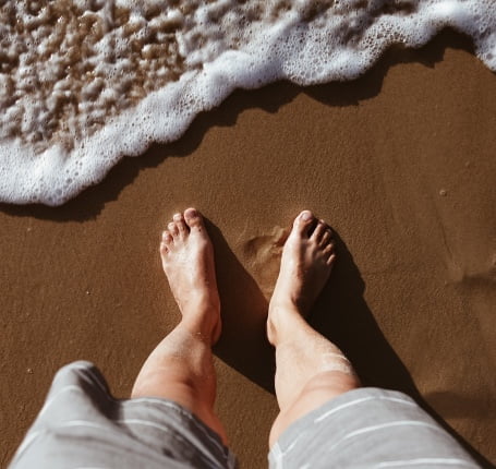 A person standing on the beach with their feet in the sand.