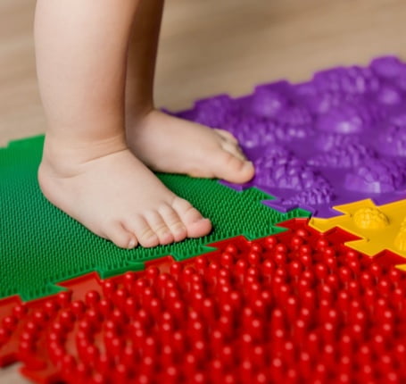 A child 's feet standing on the floor next to a mat.